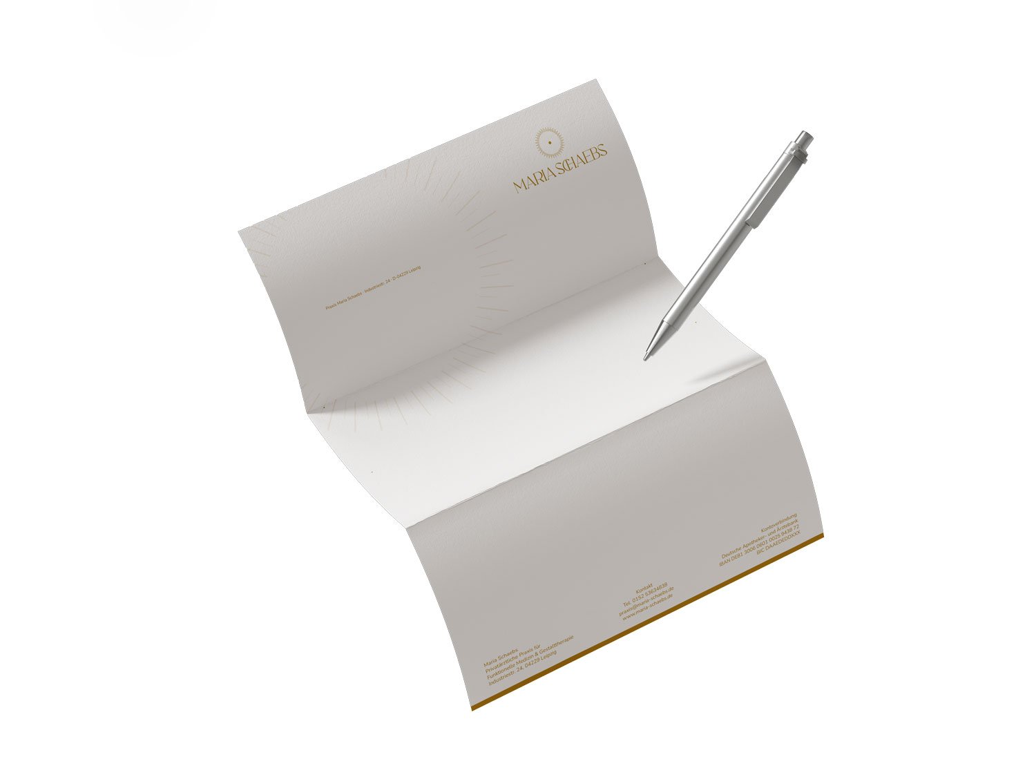 Gedruckter Praxis-Briefbogen von Maria Schaebs mit goldenem Sonnen-Logo, edler Typografie und dezenten Strahlen-Wasserzeichen im Briefkopf, präsentiert mit Kugelschreiber.