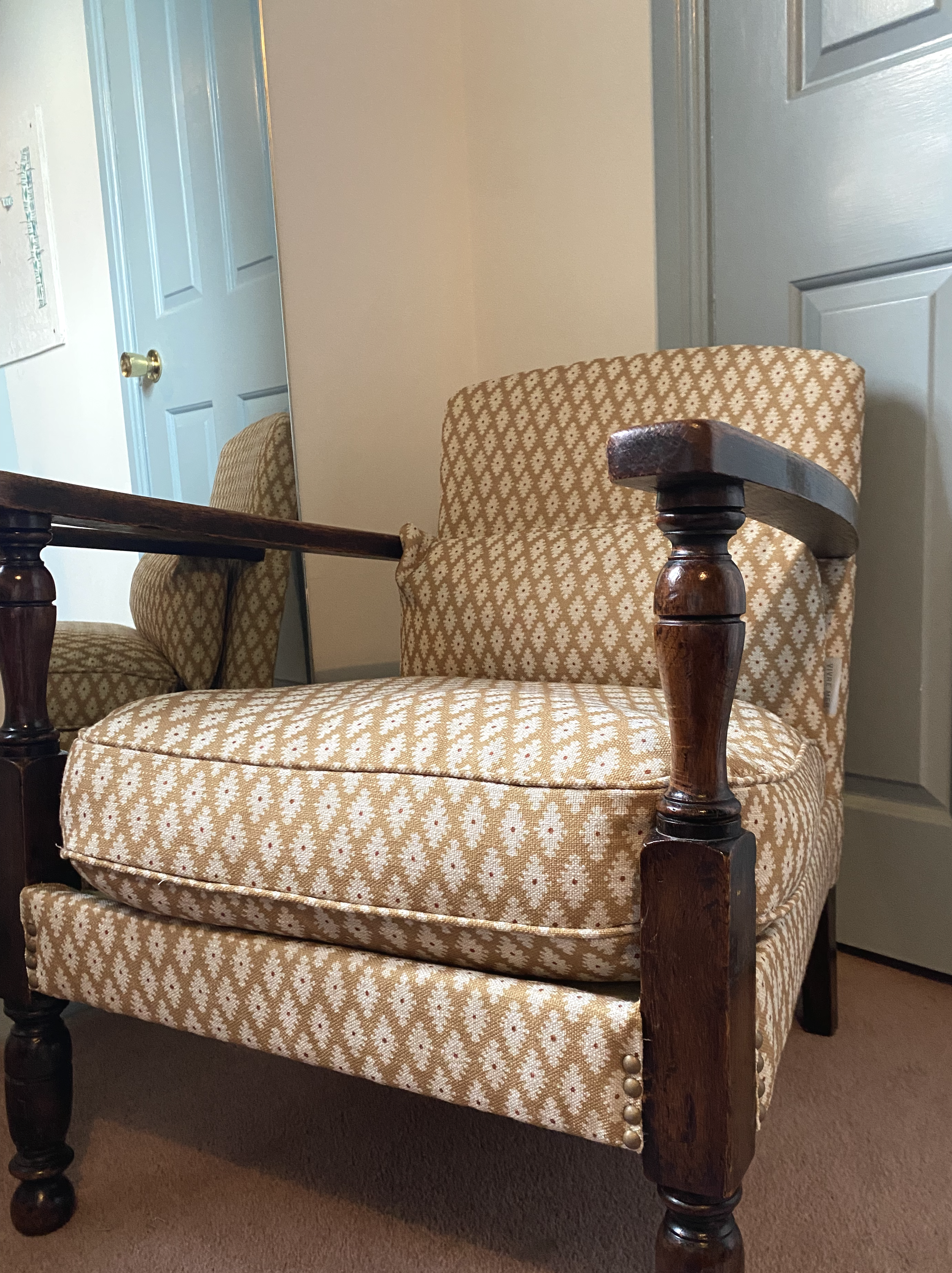 Close-up of a beige upholstered vintage armchair with wooden accents and carved floral design, with sunlight casting a shadow on the fabric.