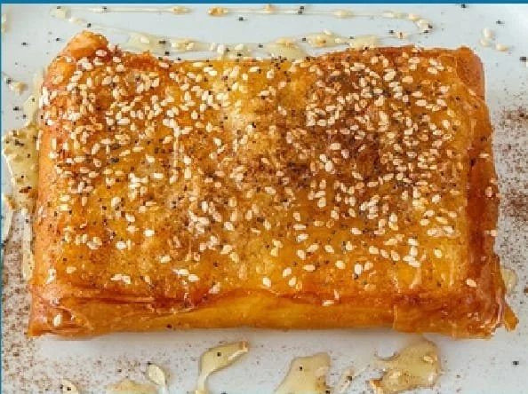 Golden brown dessert pastry topped with pearl sugar, drizzled with white chocolate, on a white plate.