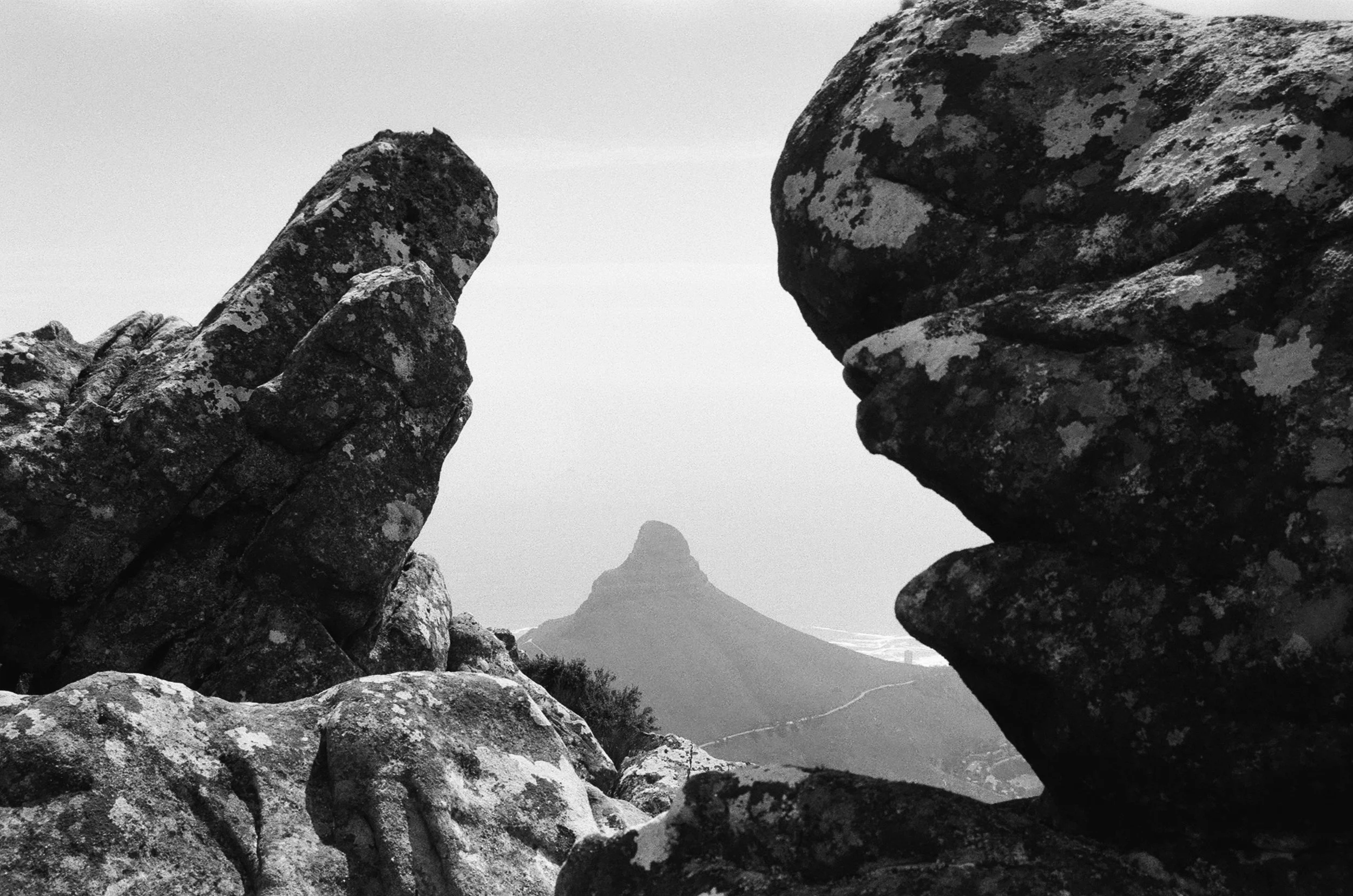 Black and white landscape photo of large weathered rocks in the foreground with a mountain peak in the background, featuring a distinctive, rounded summit.
