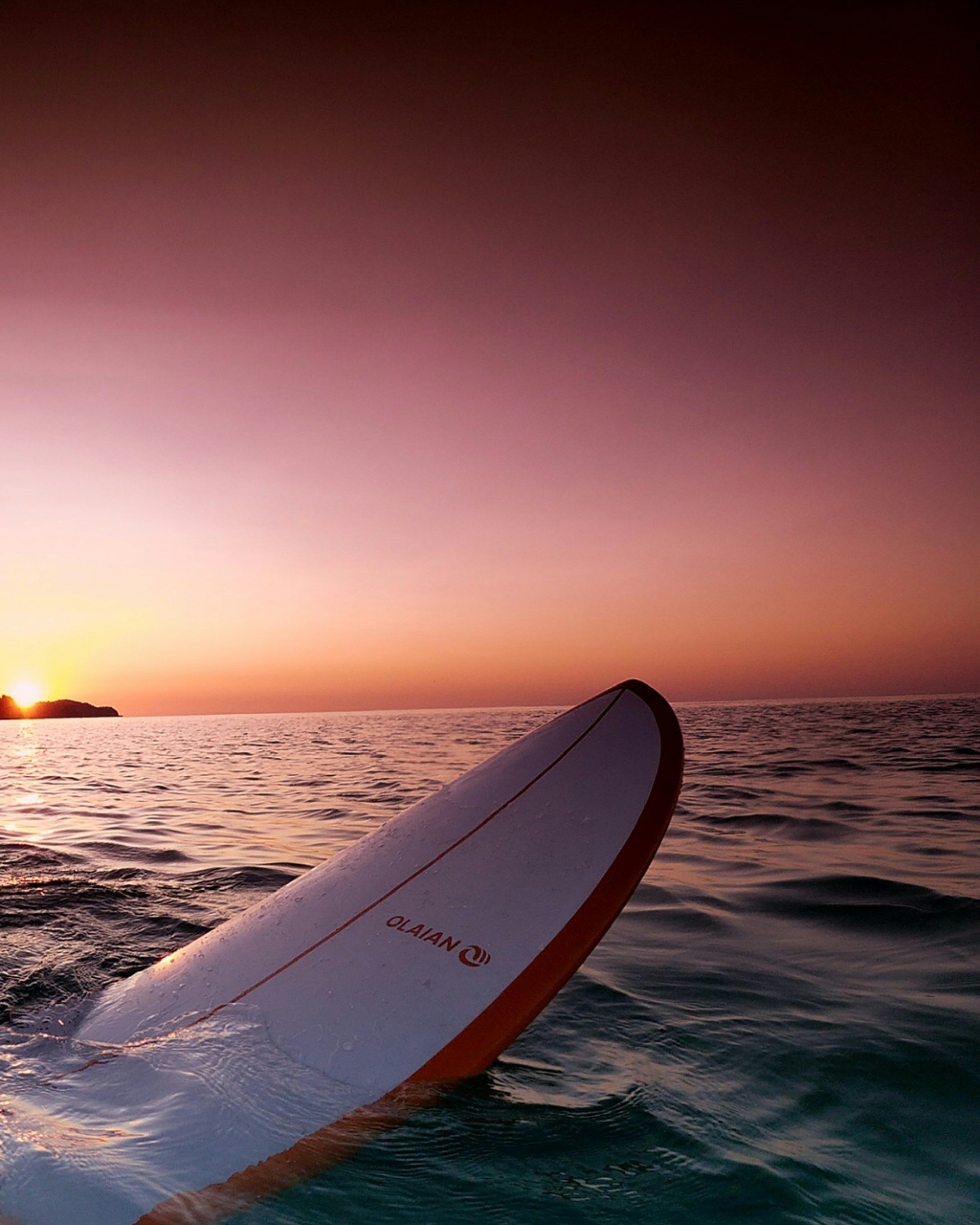 Sunset over the ocean with a surfboard partially submerged in the water. surfing In cape Town, South Africa