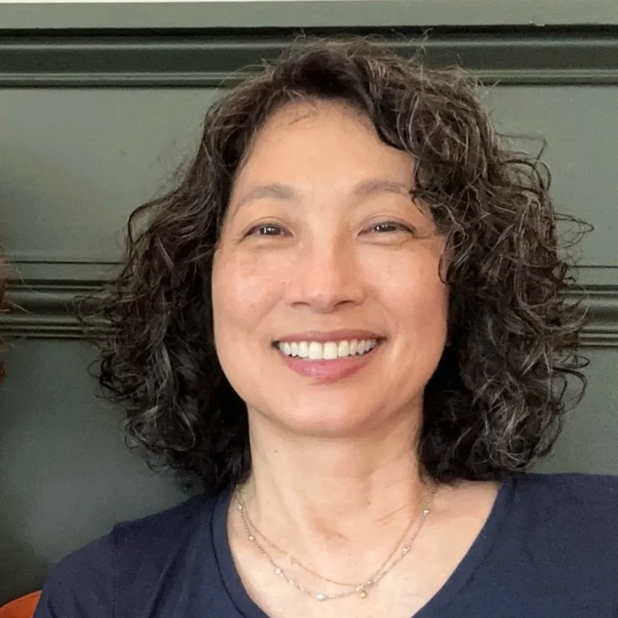 Erica Ando, PhD, co-founder of INTERVAL PAPER — smiling in front of a dark green background