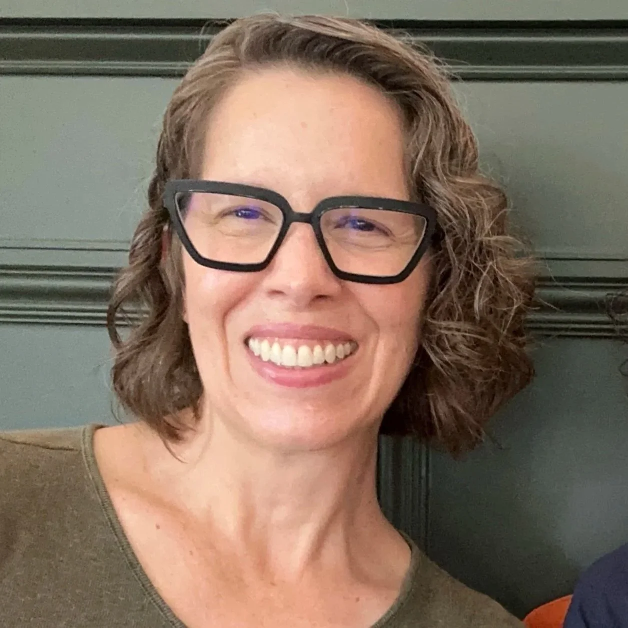 Michelle A M Miller, co-founder of INTERVAL PAPER — smiling in front of a dark green background