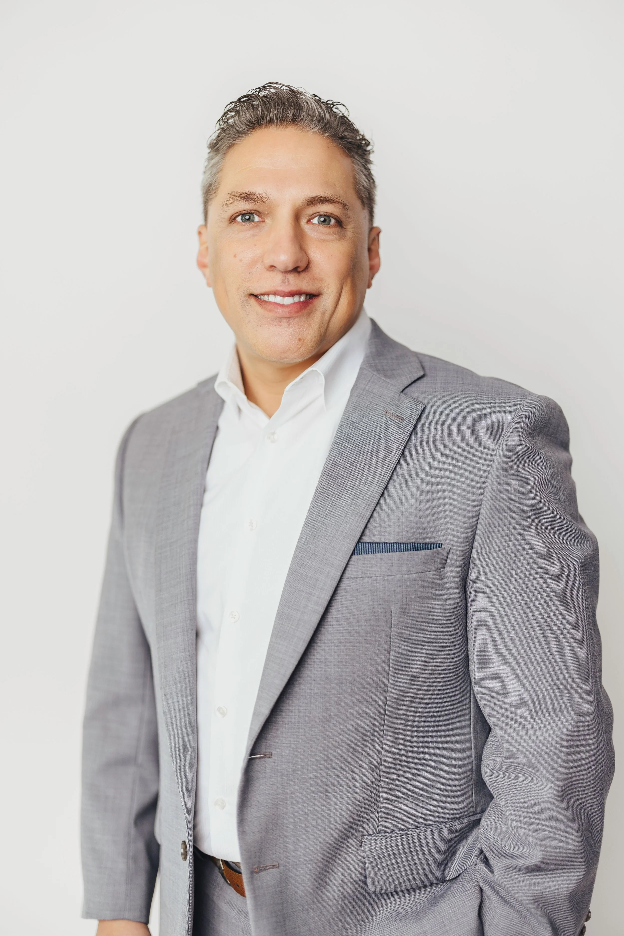 A professional man in a gray suit and white shirt smiling against a plain white background.