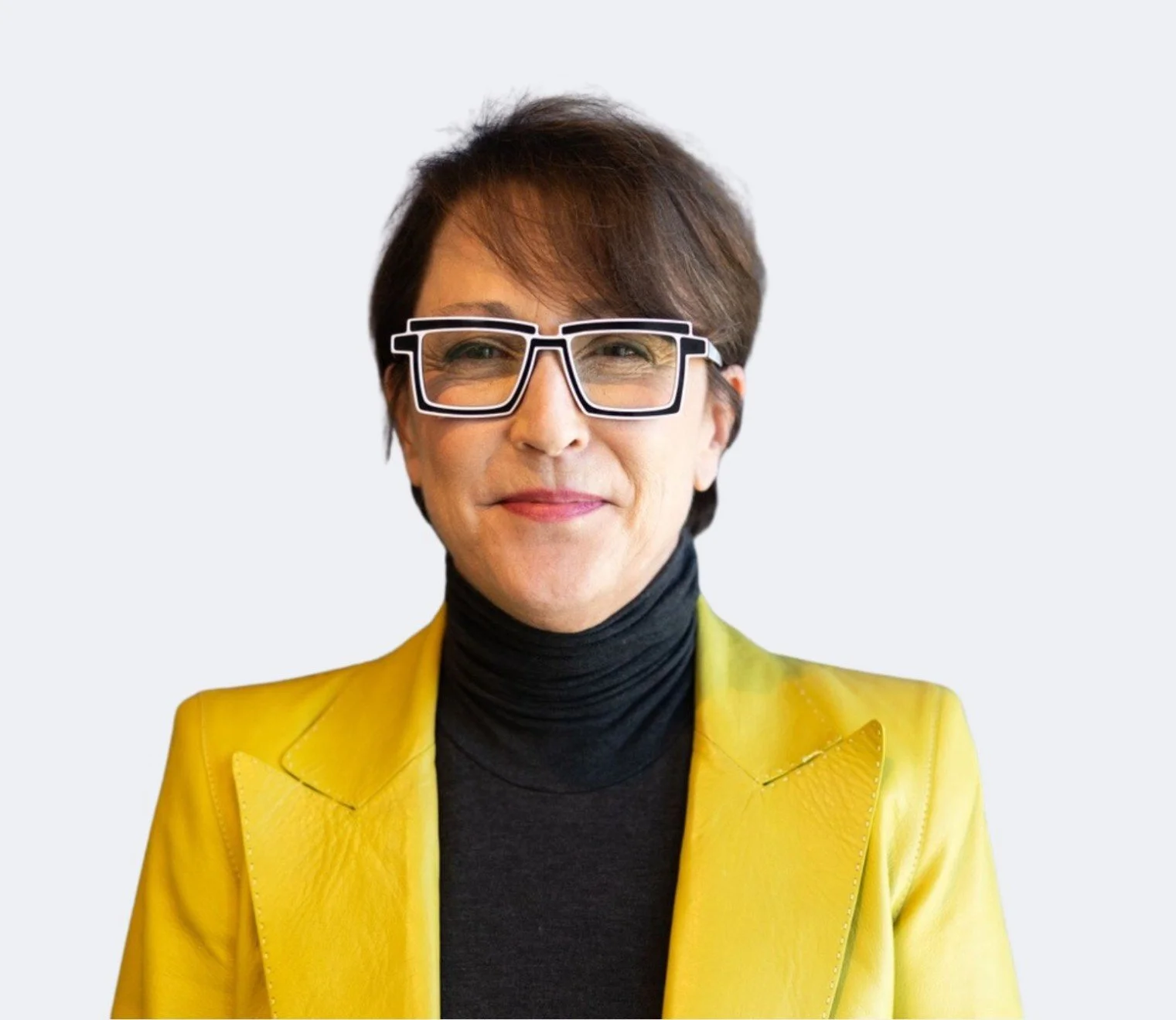 A woman with short brown hair, wearing black-rimmed glasses, a black turtleneck, and a bright yellow blazer, smiling confidently against a light gray background.