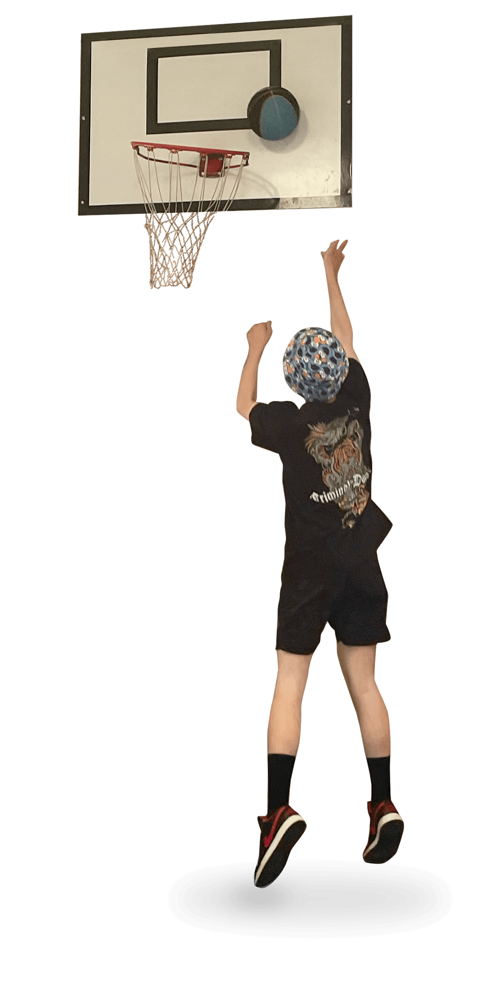 A young person with a patterned bucket hat, black t-shirt featuring a leopard, black shorts, and red sneakers is jumping in front of a basketball hoop, reaching for the ball.