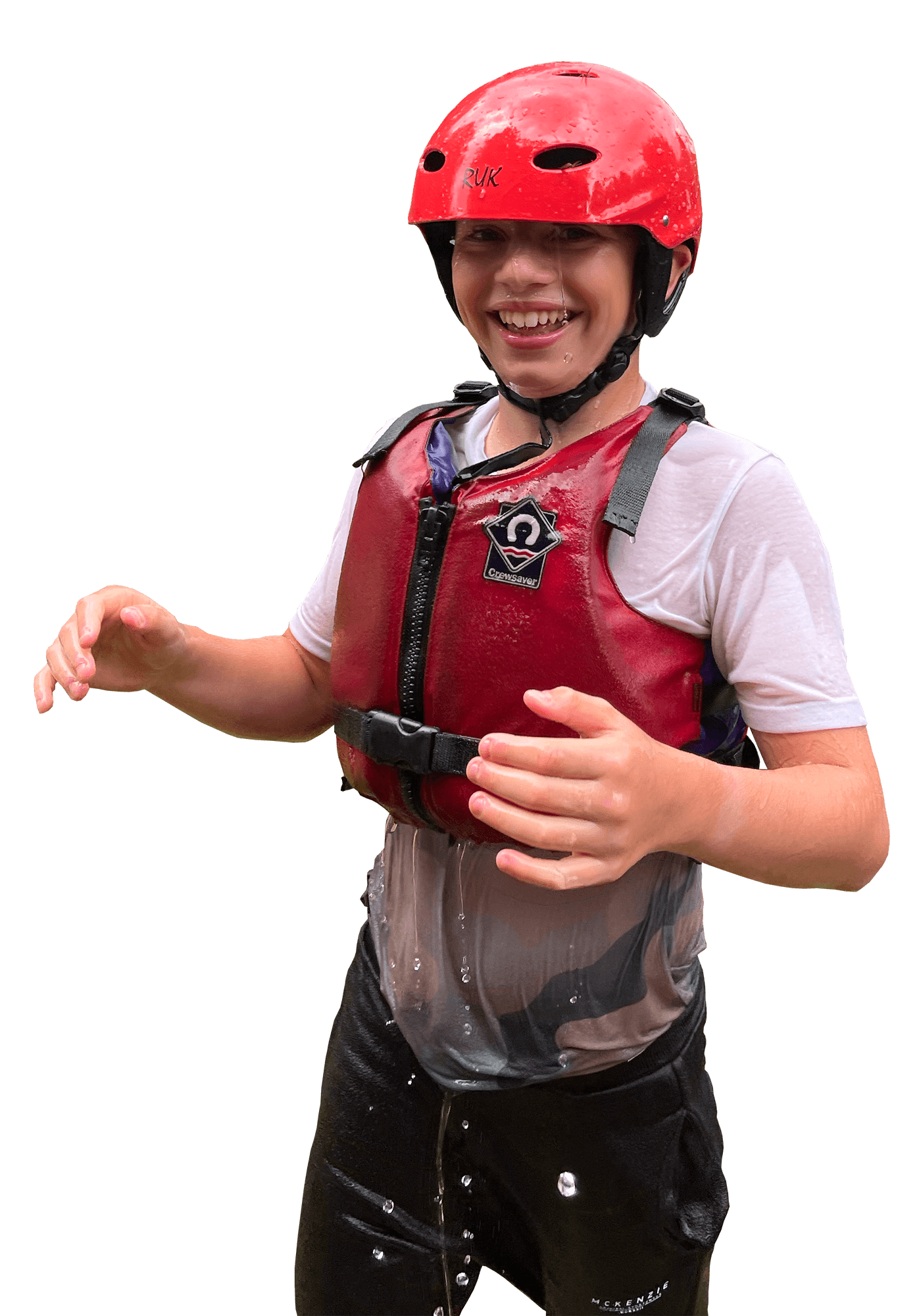 Young person smiling, wearing a red helmet and life jacket, wet from water, standing with water splashing around.