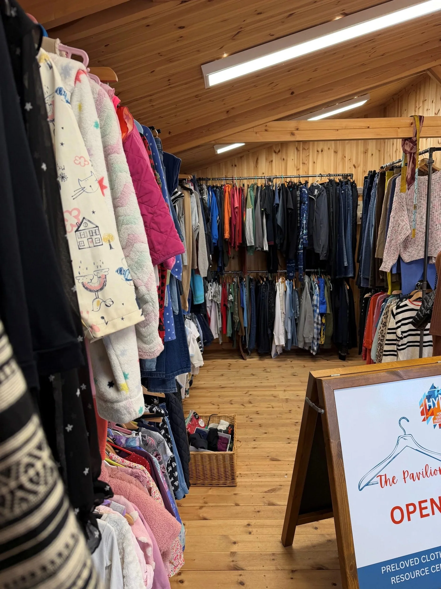 Clothing store with racks of clothes and a sign that says 'The Pavilion OPEN'