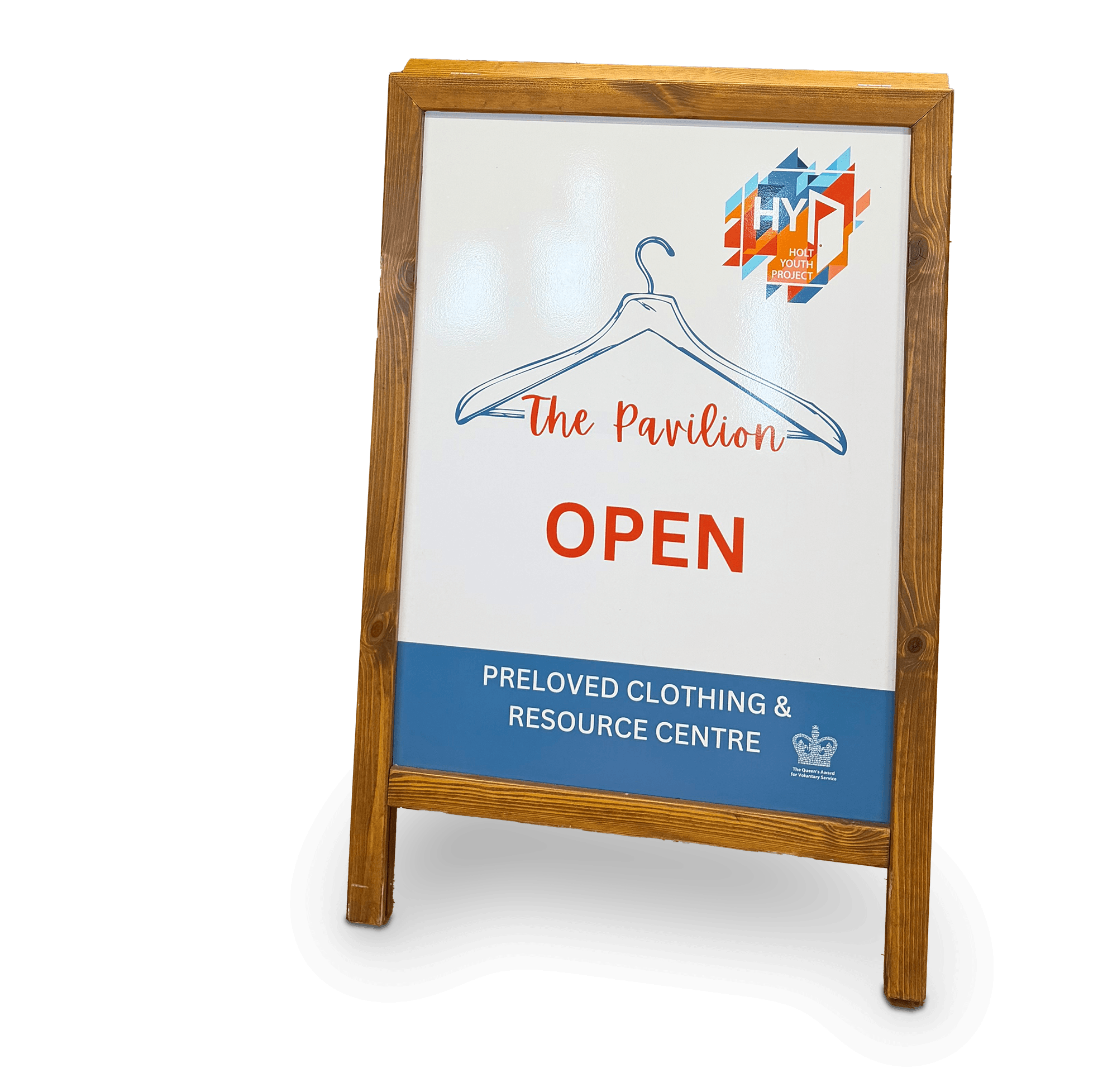 A wooden A-frame signboard with a white background displaying a logo and text for the Holt Youth Project, including the words 'The Pavilion' and 'Open' in red, with additional text about clothing and resources, and a small crown icon indicating an award.