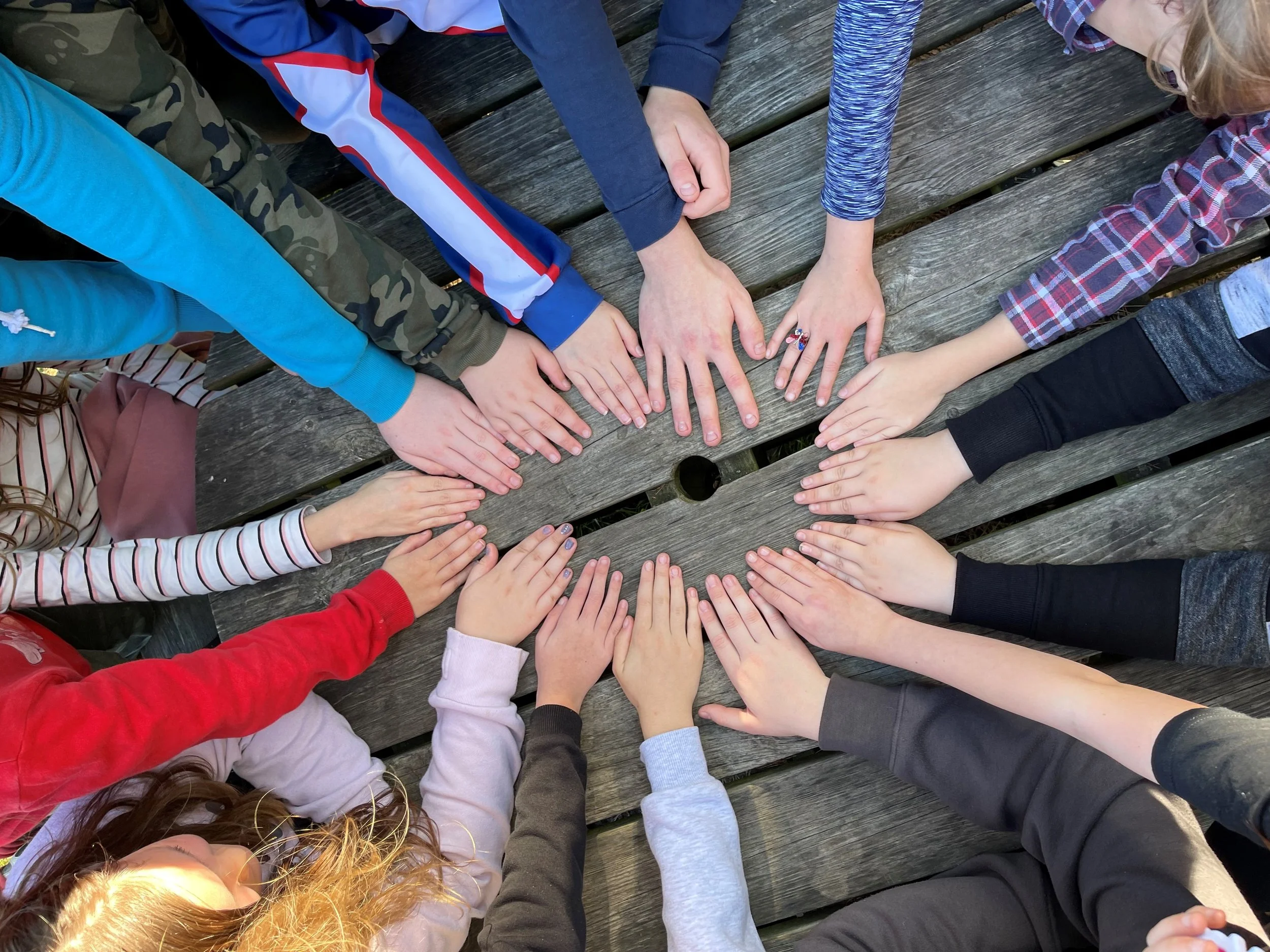 Group of children with hands stacked together on wooden outdoor table.