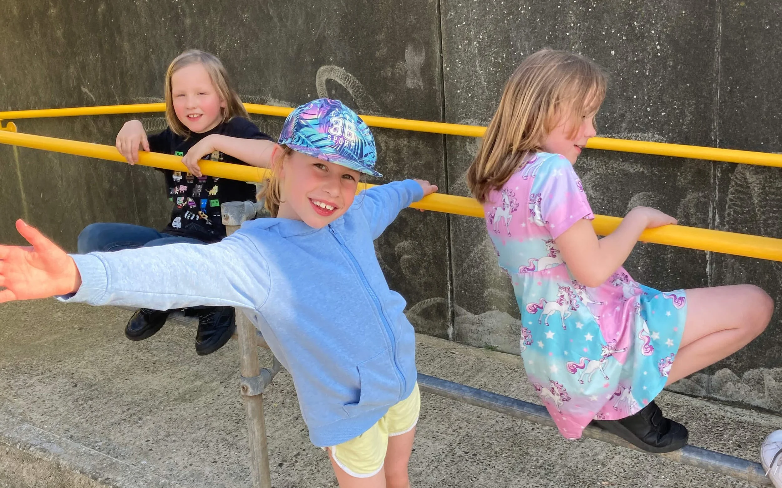 Three children playing on a balance beam outside, smiling and enjoying themselves.