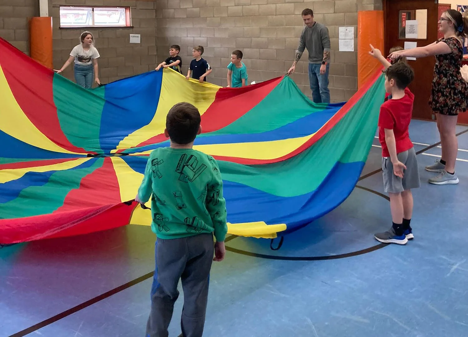 A group of children play a game with a colourful parachute in a sports hall