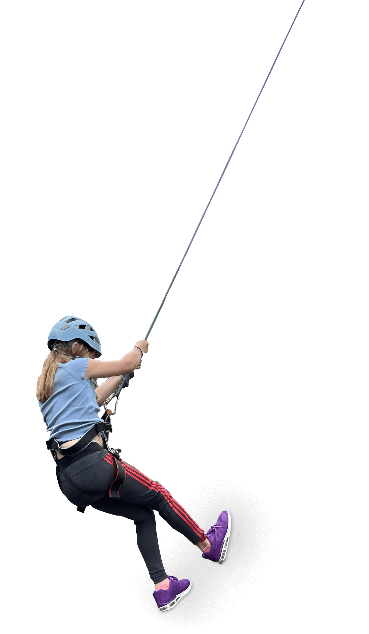 A young girl wearing a helmet and safety harness is rock climbing on an artificial climbing wall with a black background.