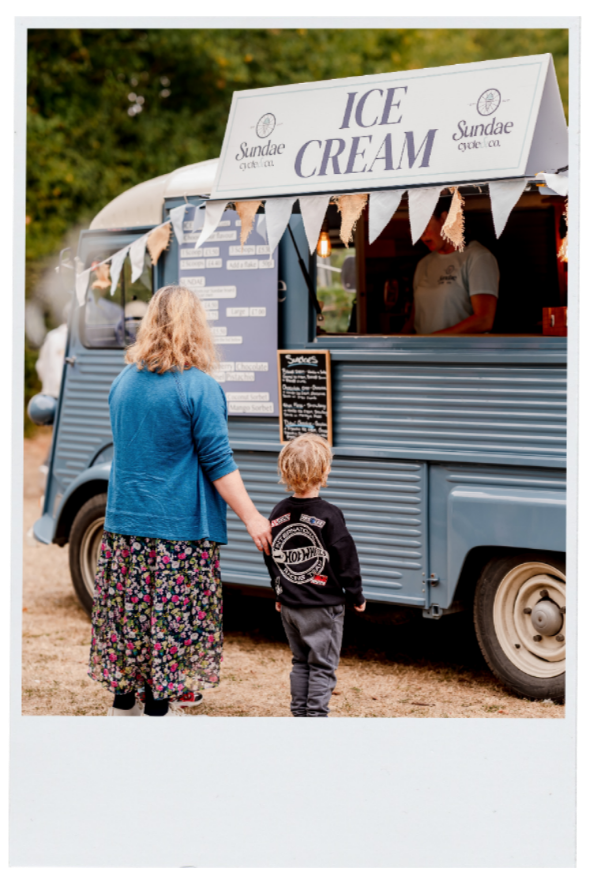 An ice cream truck serving customers at an outdoor event, with a woman and a young boy ordering from it.