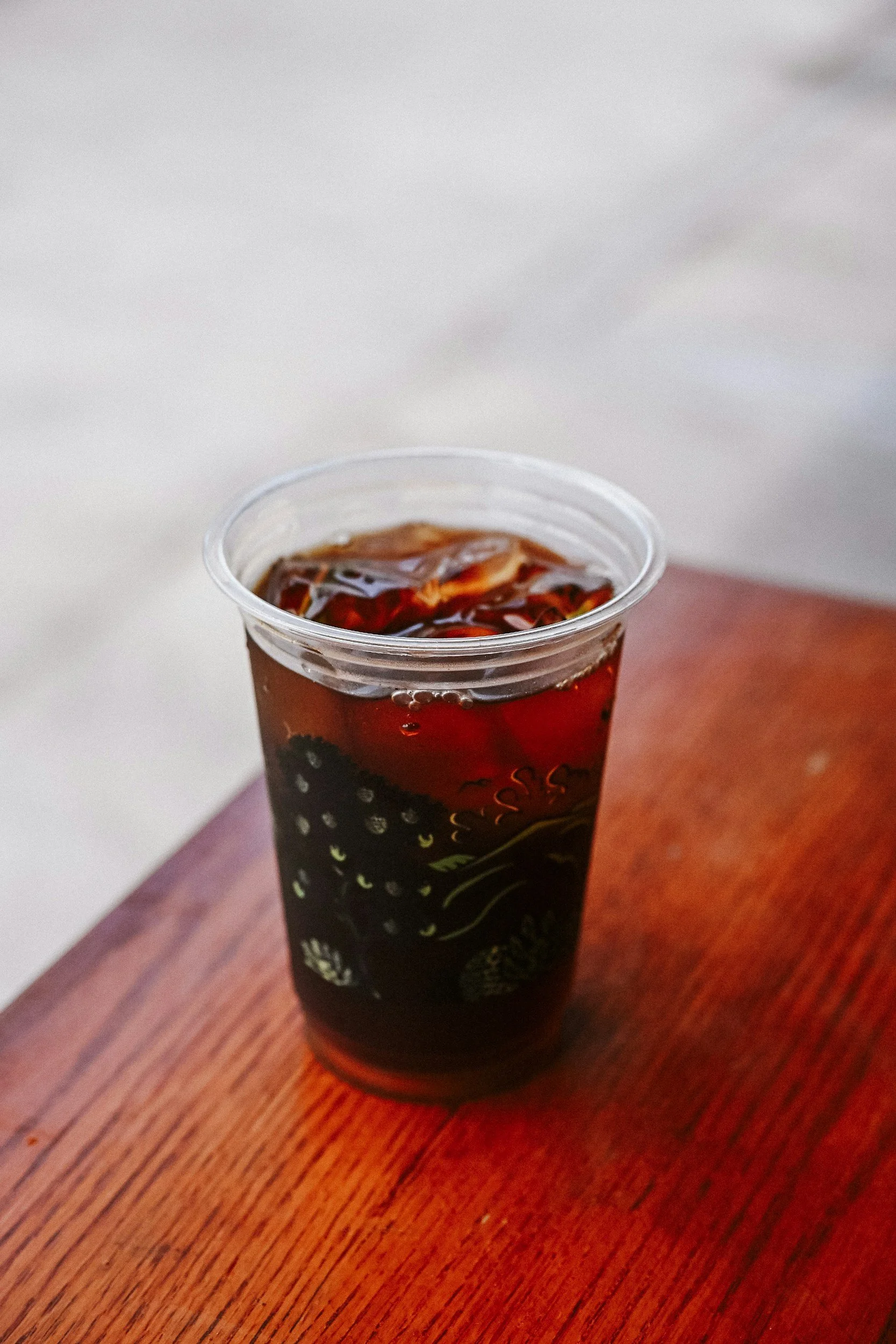 Clear plastic cup of iced dark soda on a wooden table