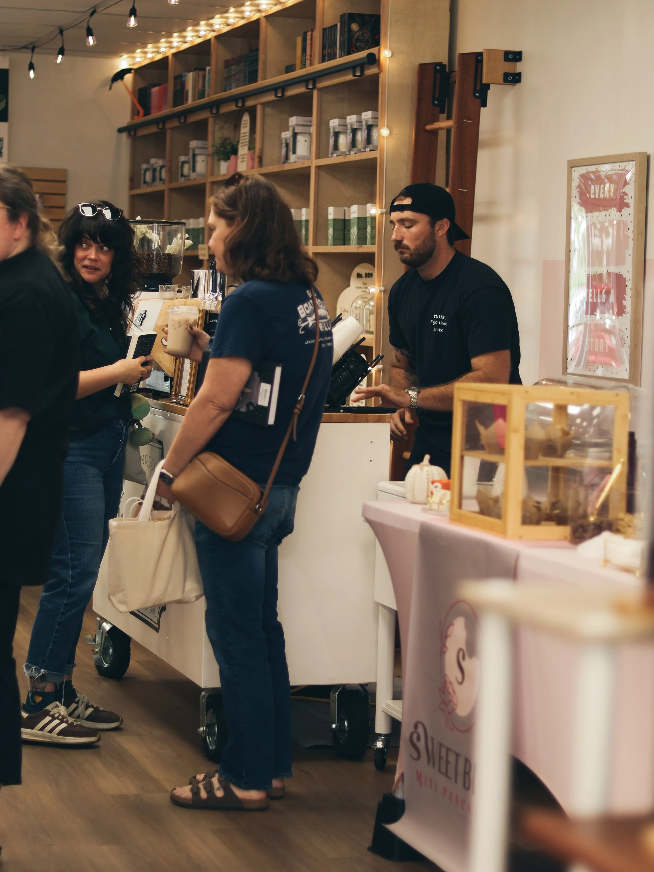 People ordering drinks at a warmly lit coffee cart, with coffee equipment in a cozy venue.