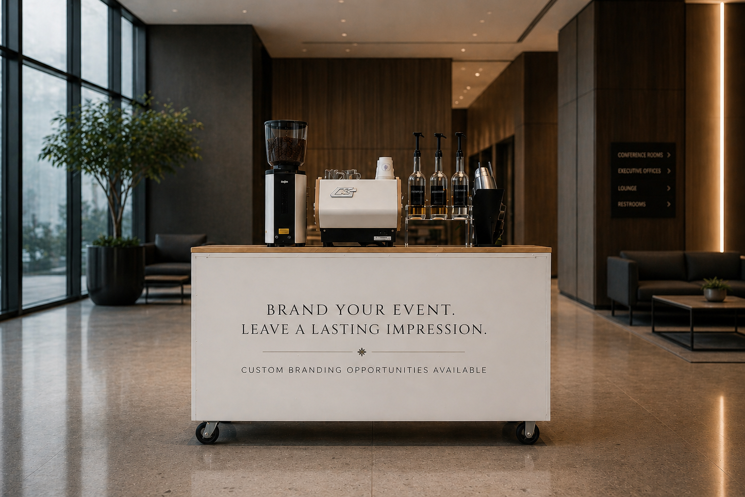 A mobile event branding station with a coffee setup inside a modern building lobby. The station has a sign that reads 'Brand Your Event. Leave a Lasting Impression. Custom Branding Opportunities Available', and coffee machines, bottles, and cups on t