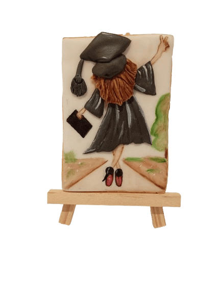 Decorative sculpture of a girl in a graduation cap and gown jumping on a path with trees.