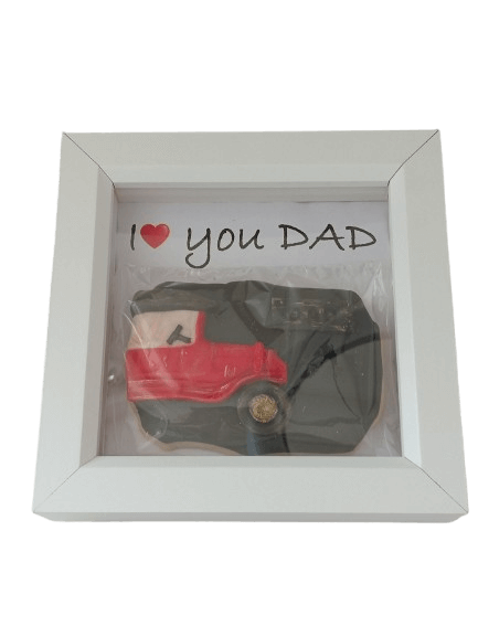 A framed cookie shaped like a fire truck with a handwritten note that says 'I love you DAD' and a red heart symbol.