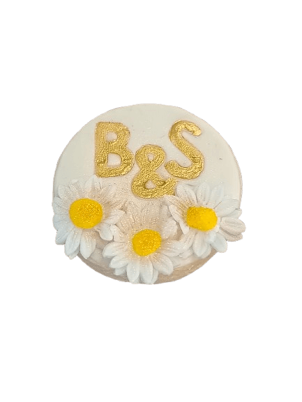 Round white cake with gold lettering 'B & S' and decorated with white daisies with yellow centers.
