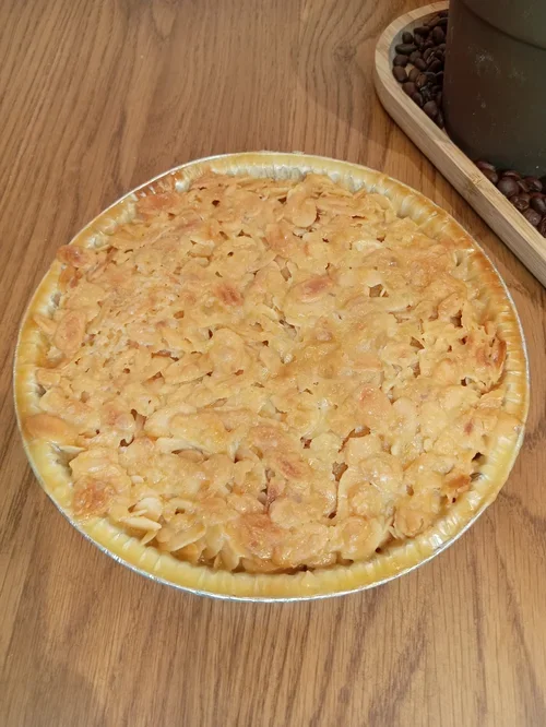 A homemade apple cobbler with a golden-brown crumbly topping in a round baking dish on a wooden table.