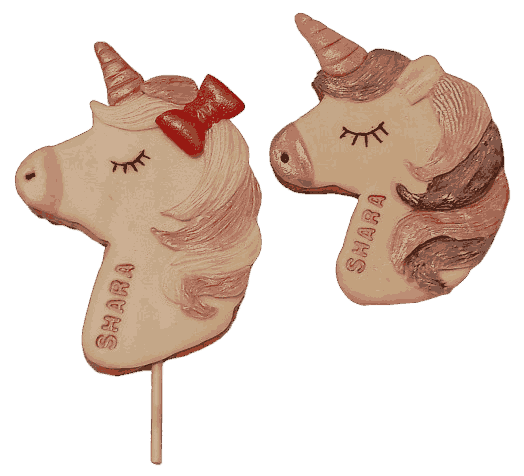 Unicorn-shaped cookies decorated with pink, brown, and red icing, one with a red bow and both with closed eyes and the name 'SHARA' written on the side.