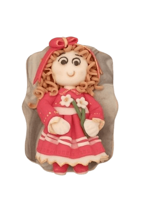 Soft plush doll of a girl with curly hair, pink dress, pink bow, and holding a flower, resting on a gray cushion.