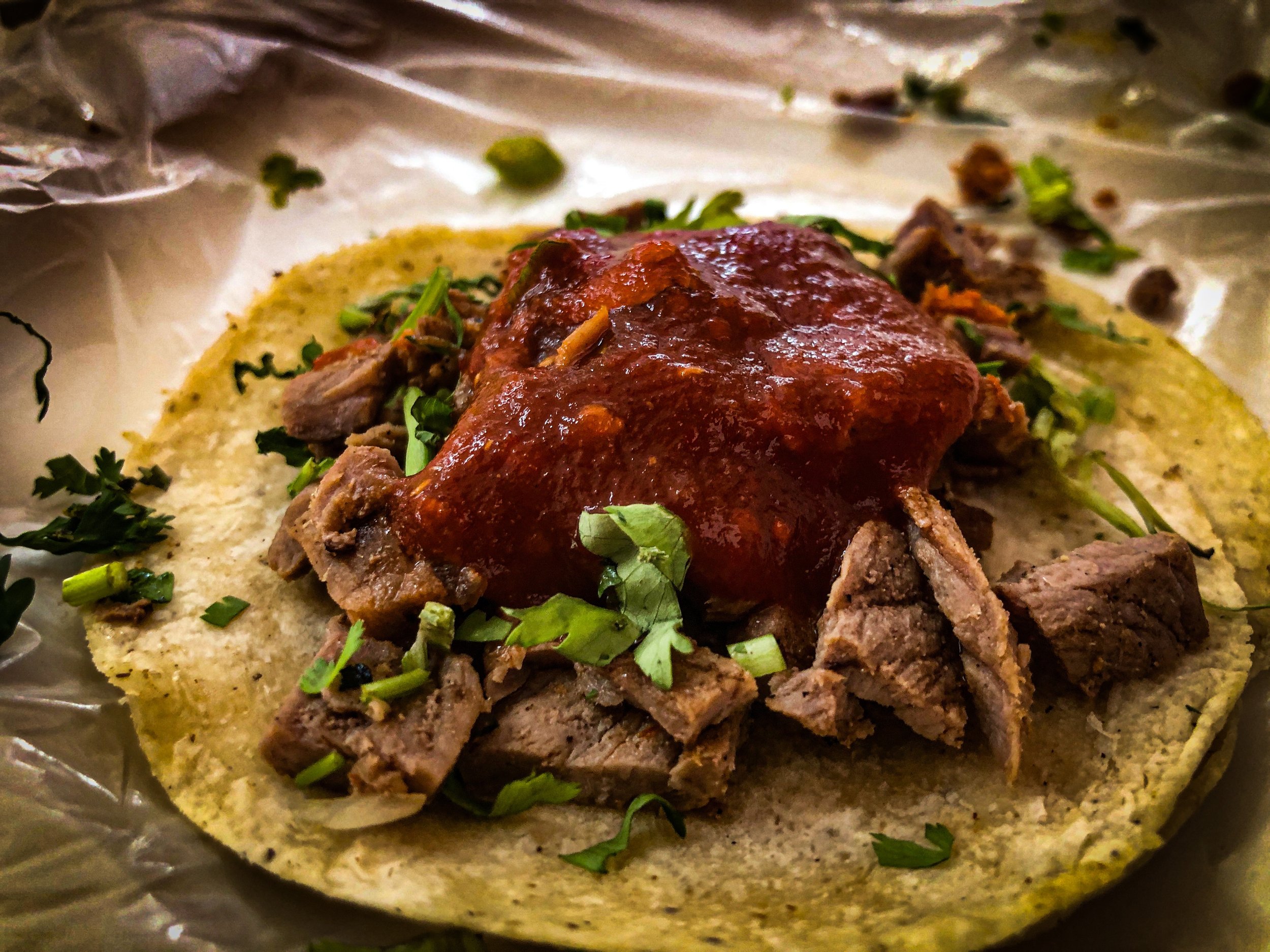 Close-up of a taco with chopped meat, cilantro, and red sauce on a corn tortilla.