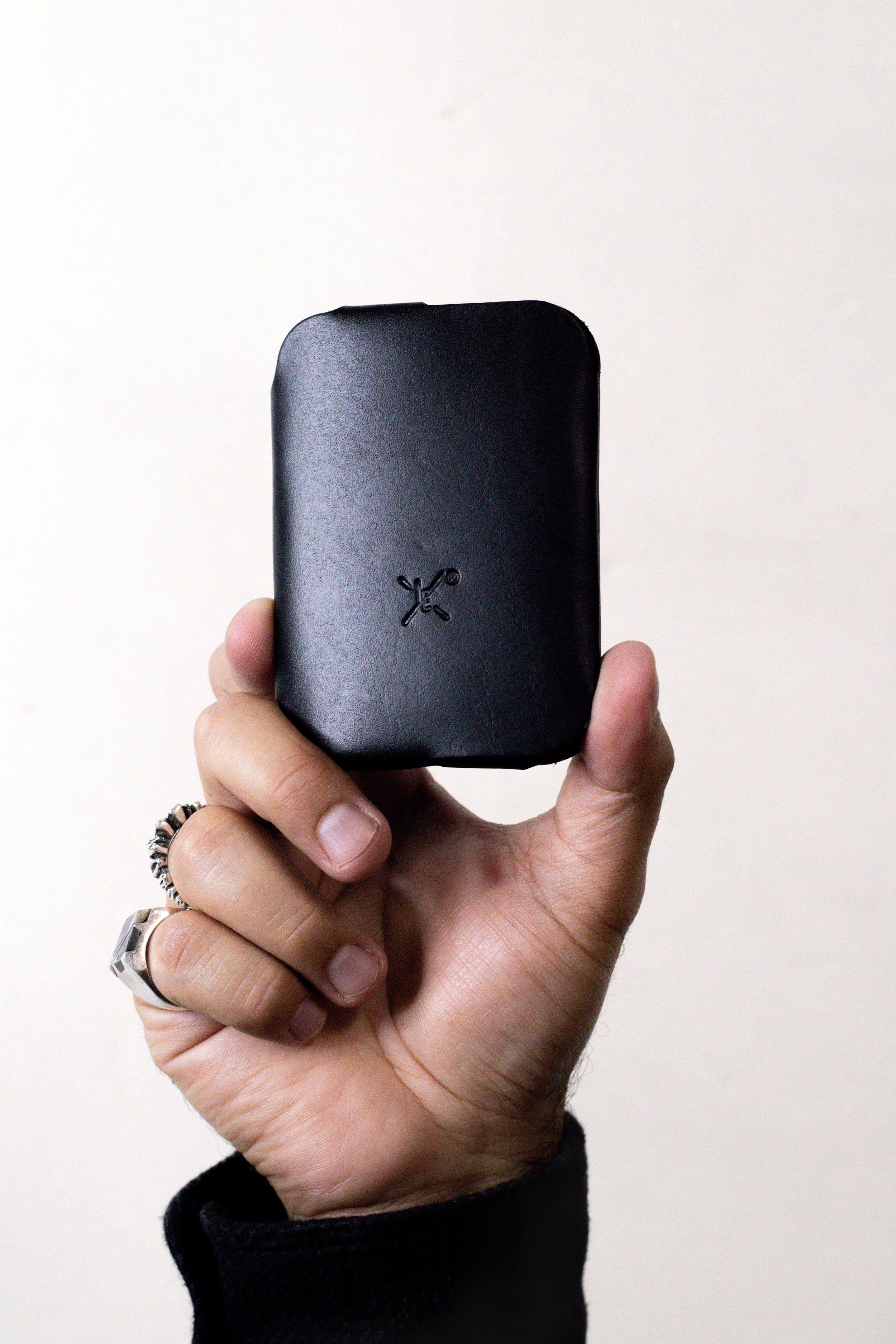 Hand holding a black wallet with a small logo, against a plain light background.