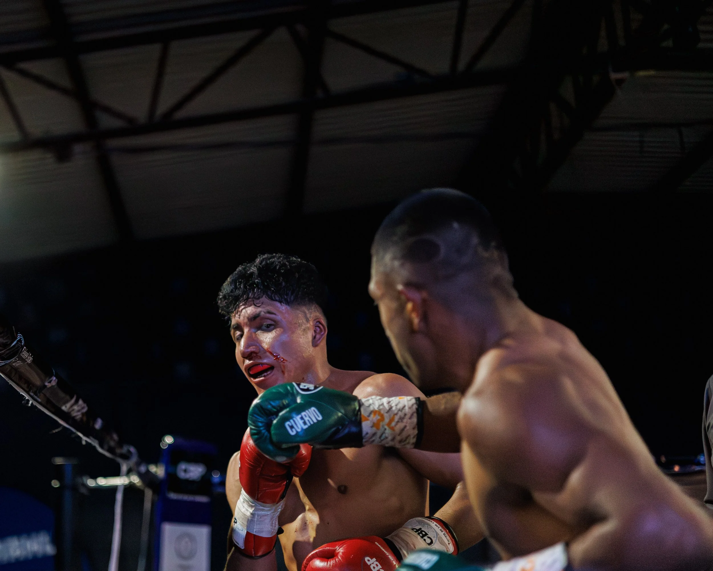 A boxing match showing two fighters in the ring. One fighter is delivering a punch to the other, who has a cut on his face.