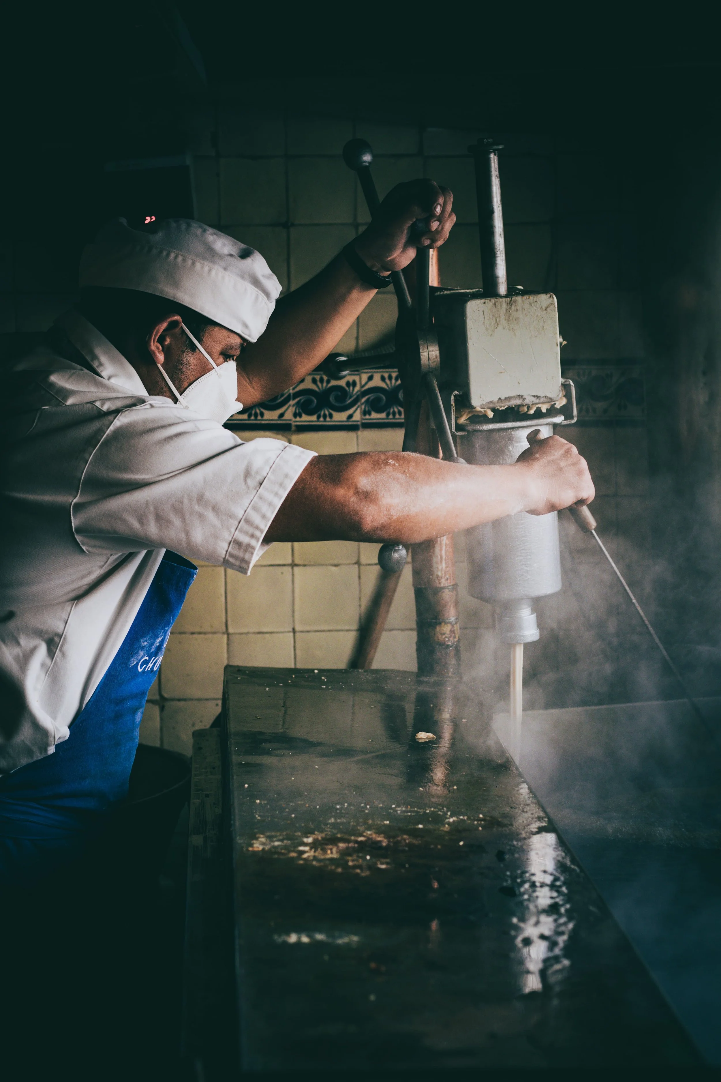 Chef wearing a white uniform, face mask, and cap preparing churros at Mexico City