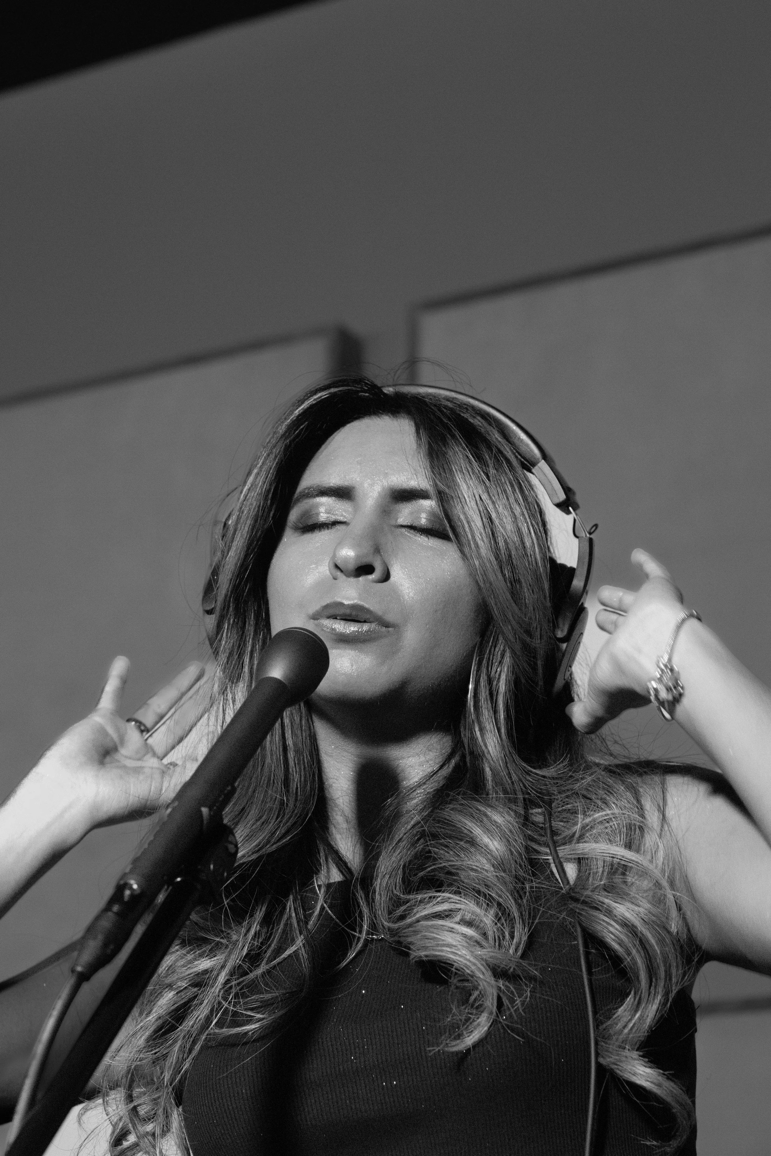 Black and white photo of a woman singing with eyes closed, wearing headphones and standing in front of a microphone.