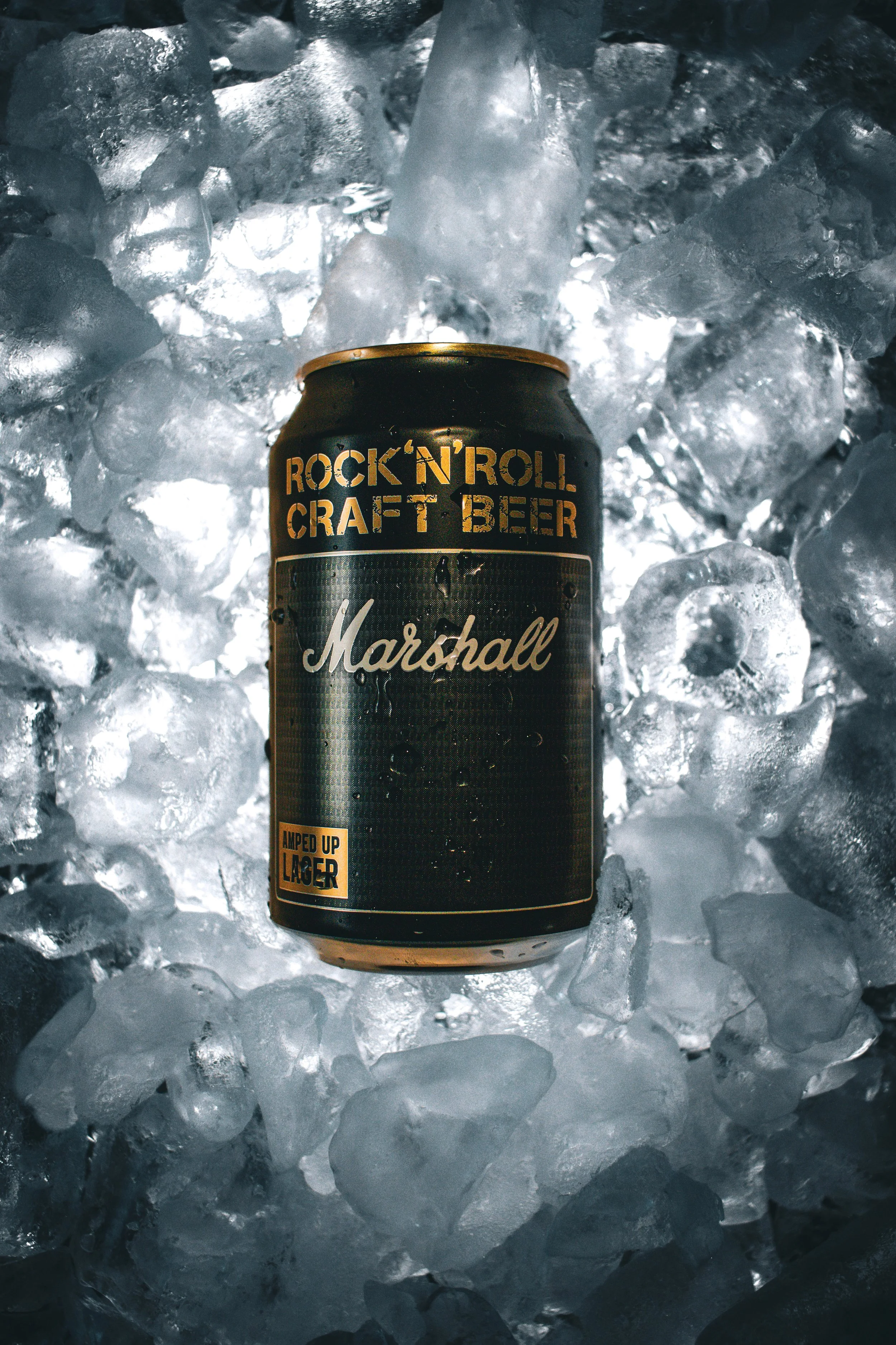 A can of Marshall beer labeled 'Rock 'N' Roll Craft Beer' and 'Amped Up Lager' resting on ice cubes.