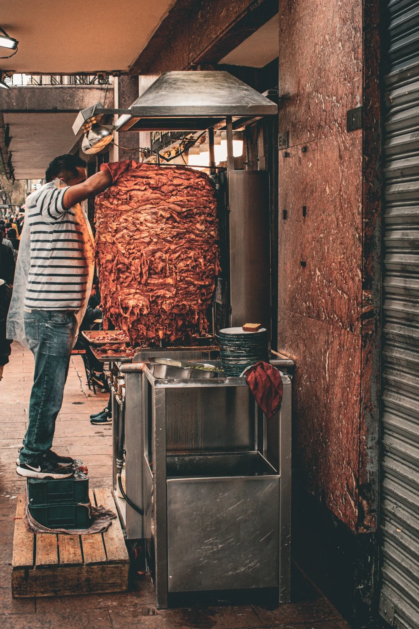 A man preparing to cut a large vertical spit of slow-cooked meat at a street food stand.