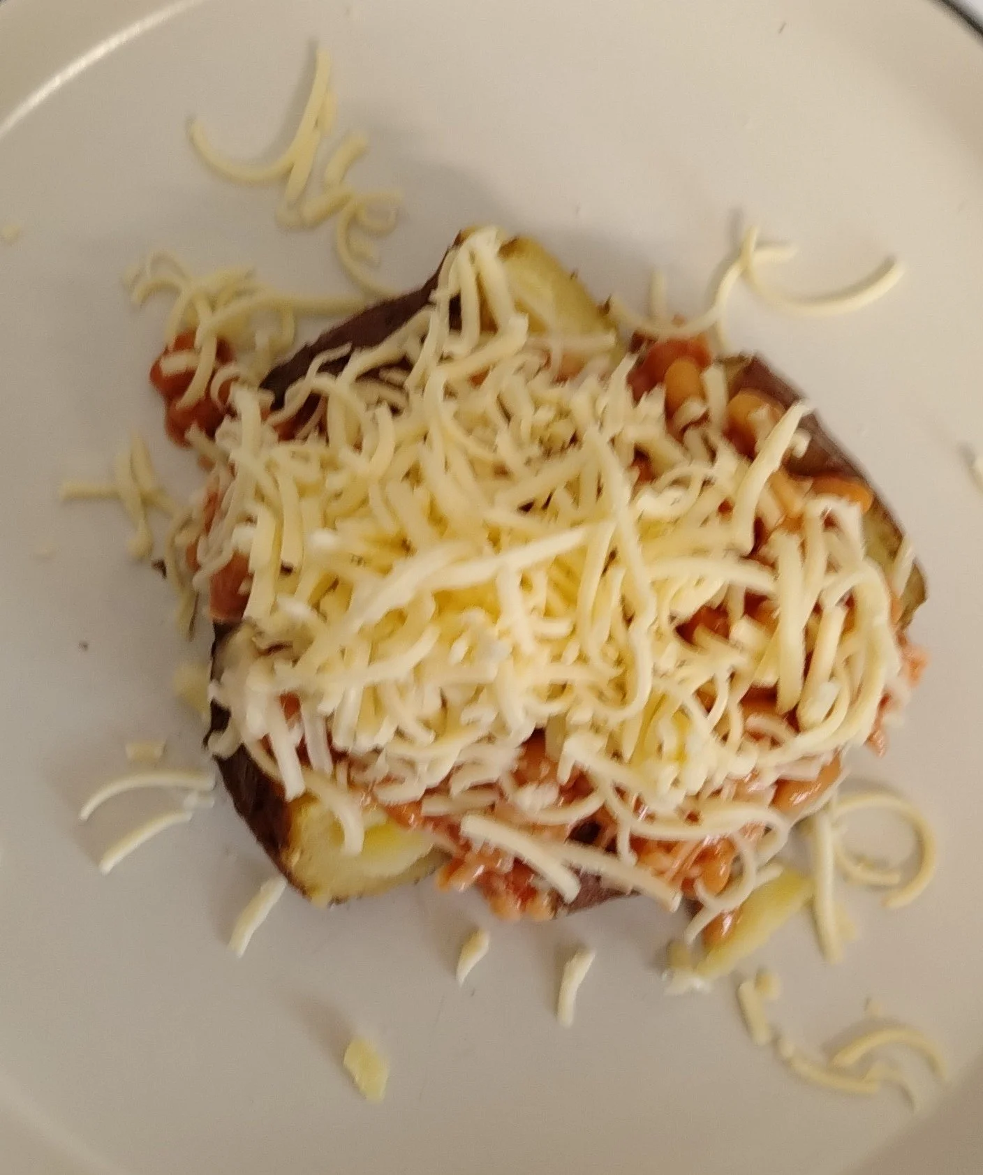 A baked potato topped with shredded cheese, sour cream, and other toppings, on a white plate.