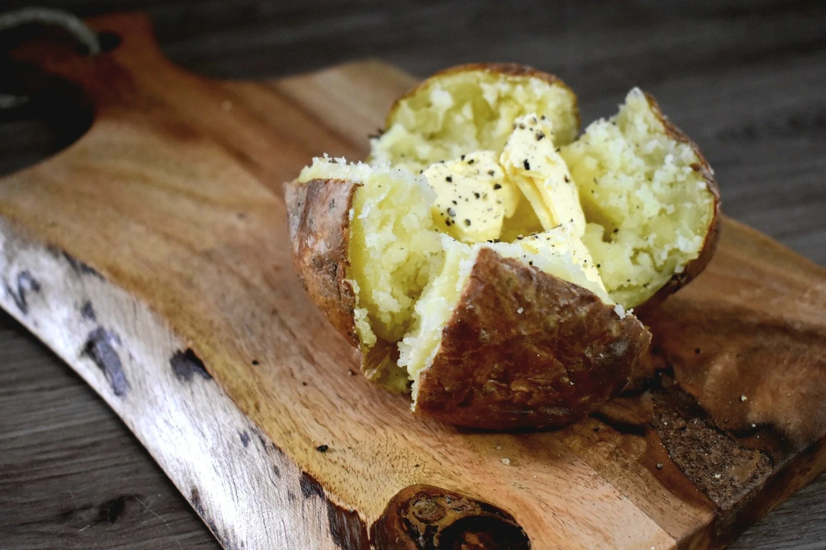 Baked potato with butter and black pepper on a wooden cutting board.