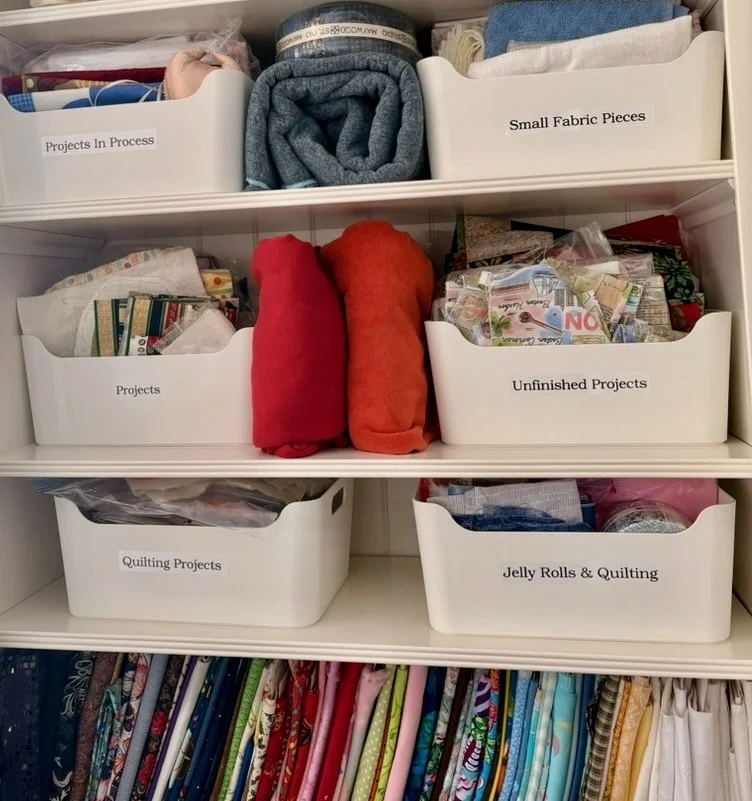 Open white bins labeled Projects In Process, Unfinished Projects, and Small Fabric Pieces on cabinet shelves
