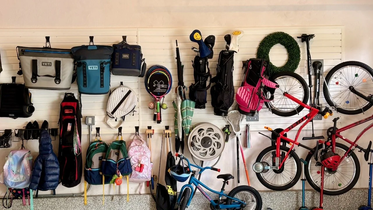 Garage wall with backpacks, bags, sports gear, and kids' bikes hung on hooks at an easy height