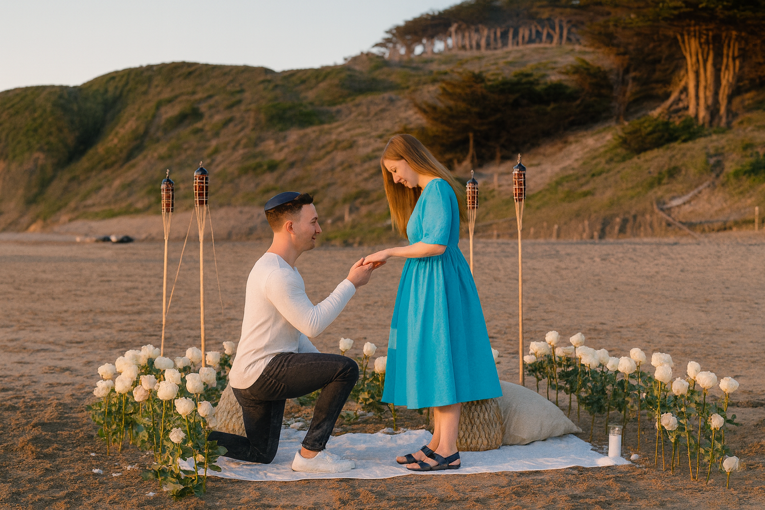 A man wearing a yarmulka, proposing to a woman on a beach during sunset with flowers, torches, and candles around them.