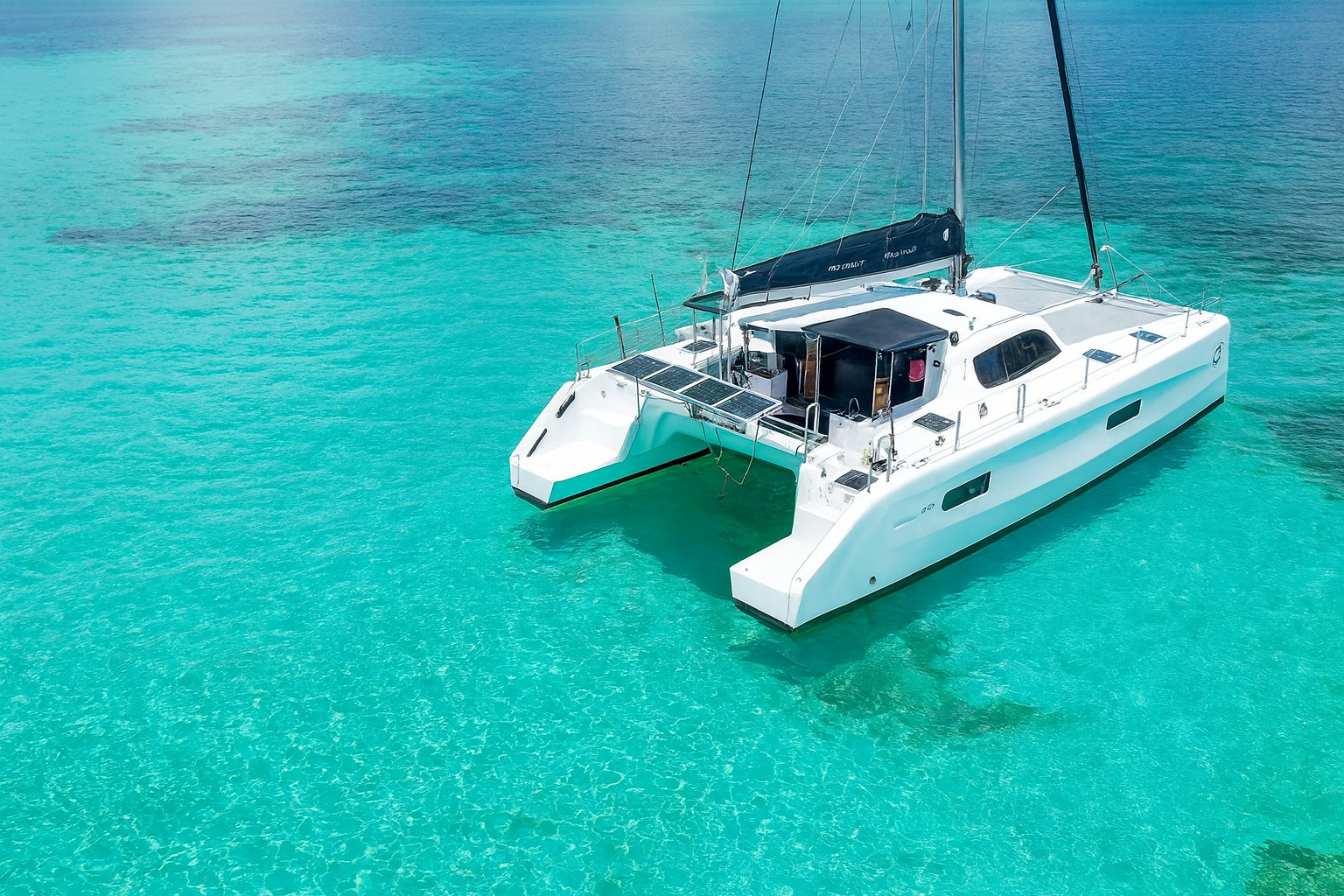 People swimming and relaxing in clear turquoise water near a white sailing catamaran with solar panels.