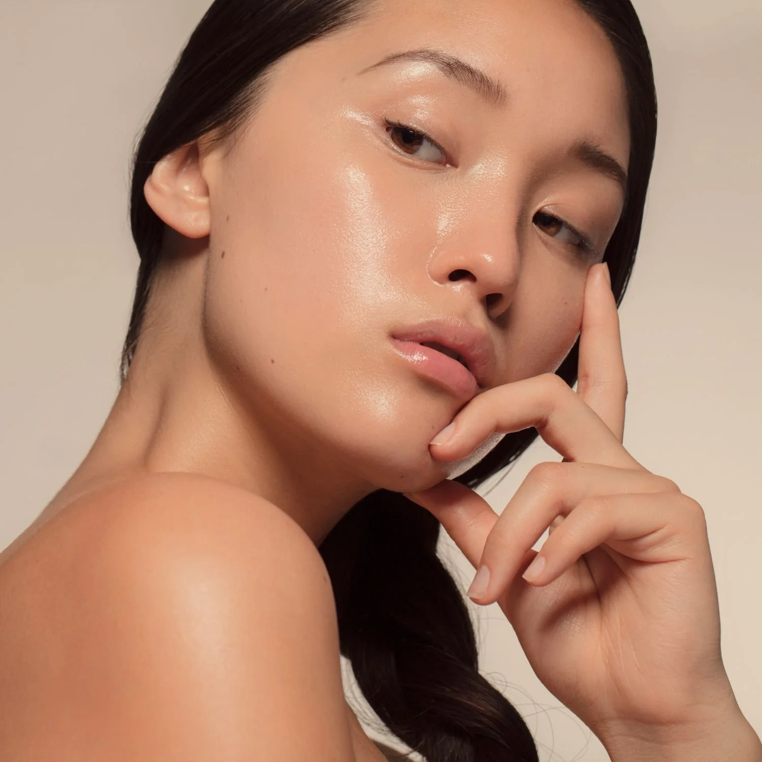 Close-up of a woman with smooth, glowing skin touching her lips with her index finger.