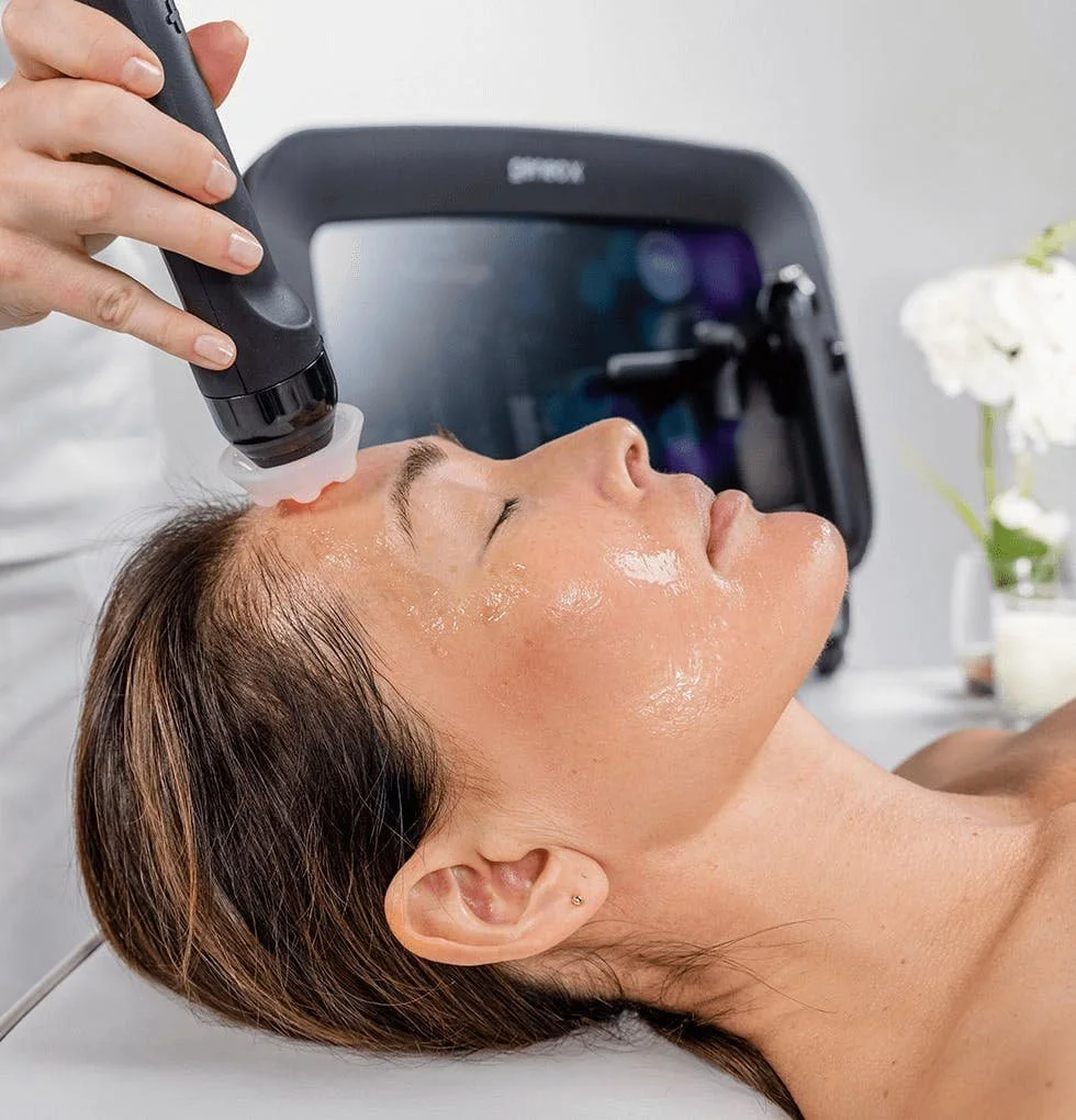 A woman receiving a facial treatment with a handheld skincare device in a spa or clinic setting.