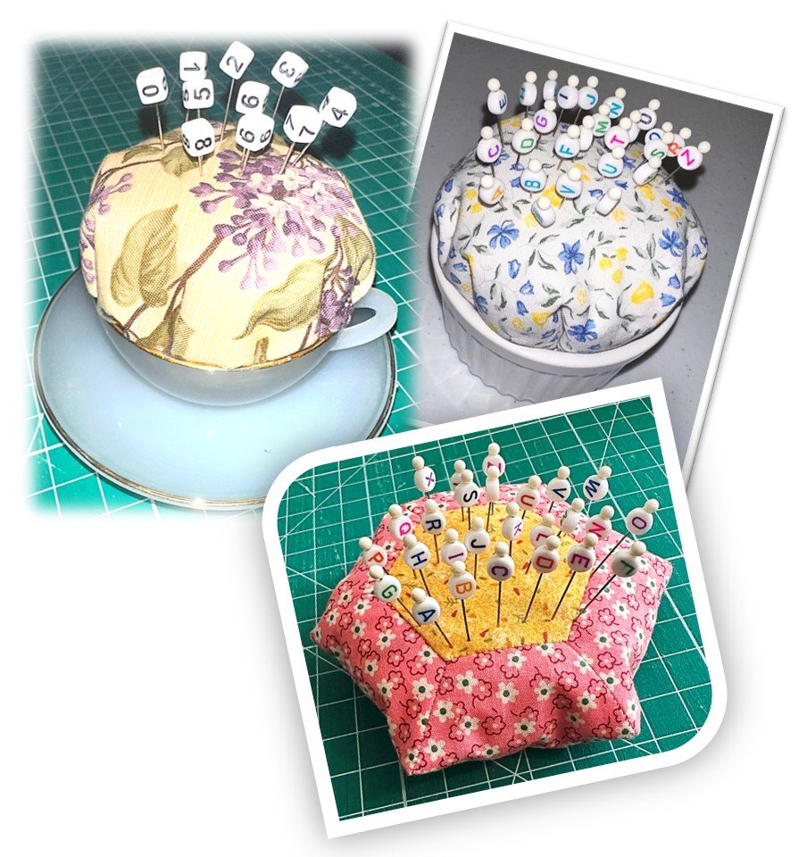 Three pincushions covered with floral fabric, each with sewing pins that have lettered or numbered white beads, arranged on a green cutting mat and a white surface.