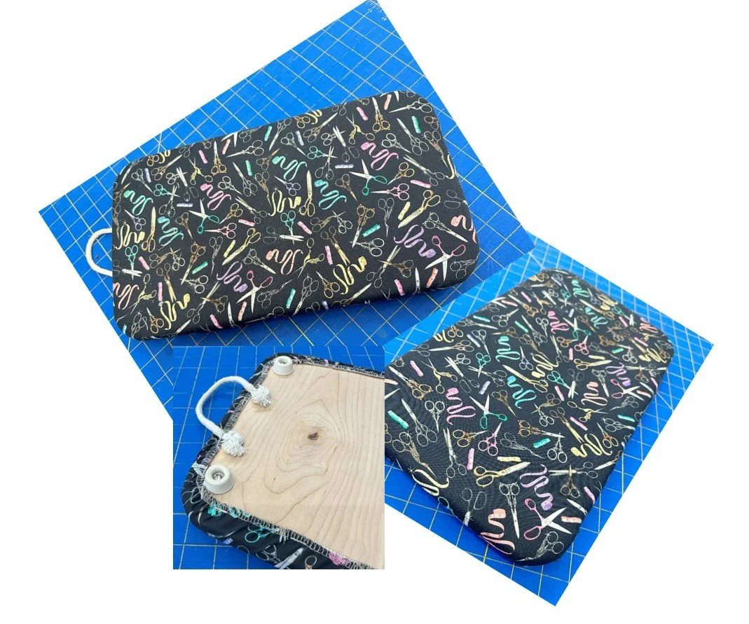 A sewing project featuring a fabric-covered item with a sewing pattern, a piece of wood with casters attached, and a cutting mat. The fabric has a pattern of colorful scissors and sewing tools.
