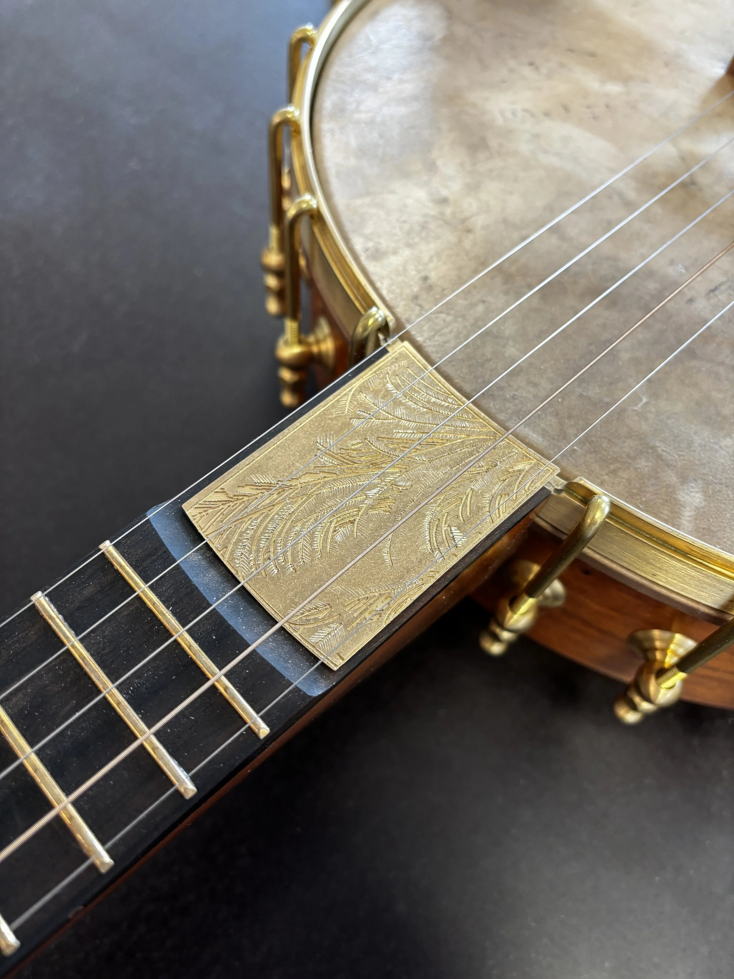 Close-up of a vintage guitar neck with gold decorative inlay, gold hardware, and four strings.