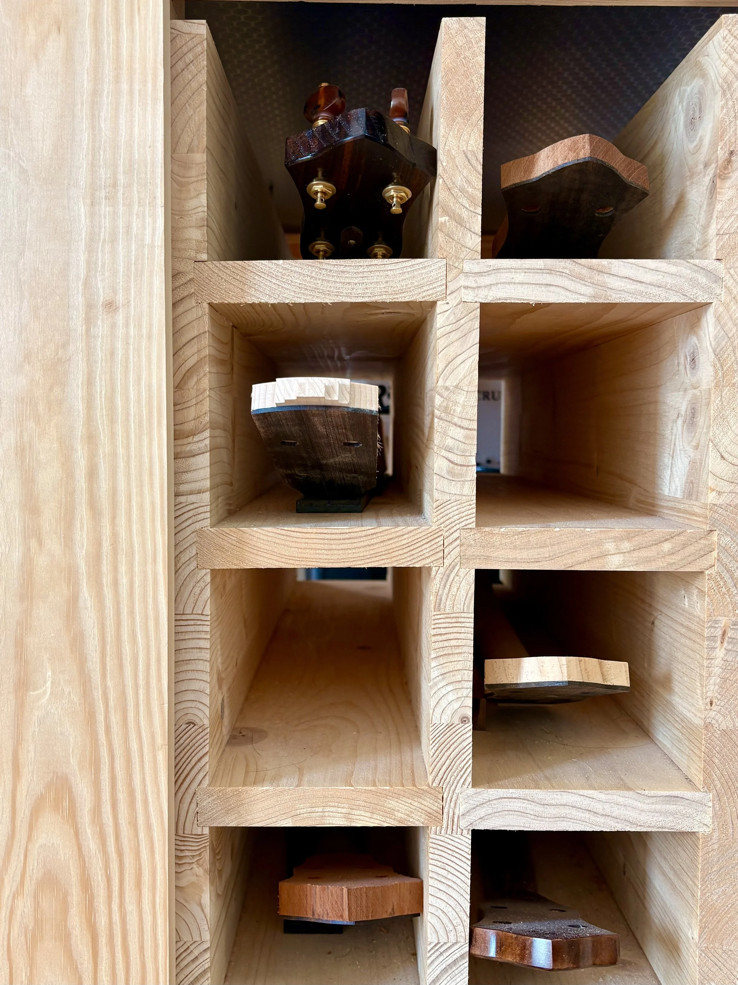 A wooden rack with multiple compartments, holding several banjo and guitar necks in progress.