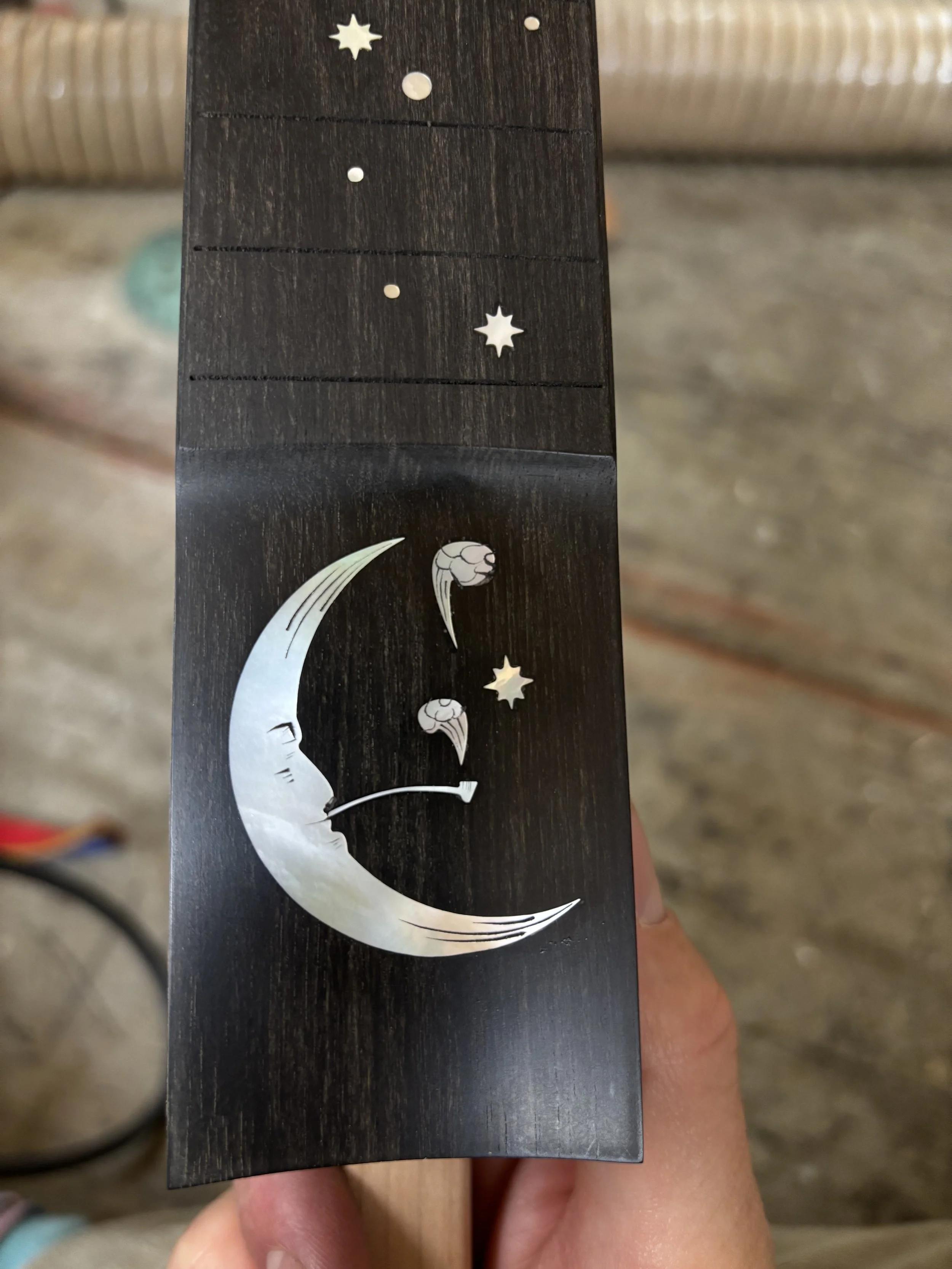A black object with a silver crescent moon playing a pipe, surrounded by small stars and planets.