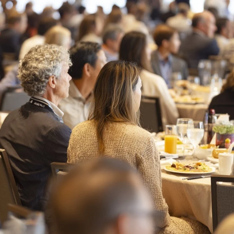 Attendees seated at tables during a conference or seminar, with food and drinks on the tables.