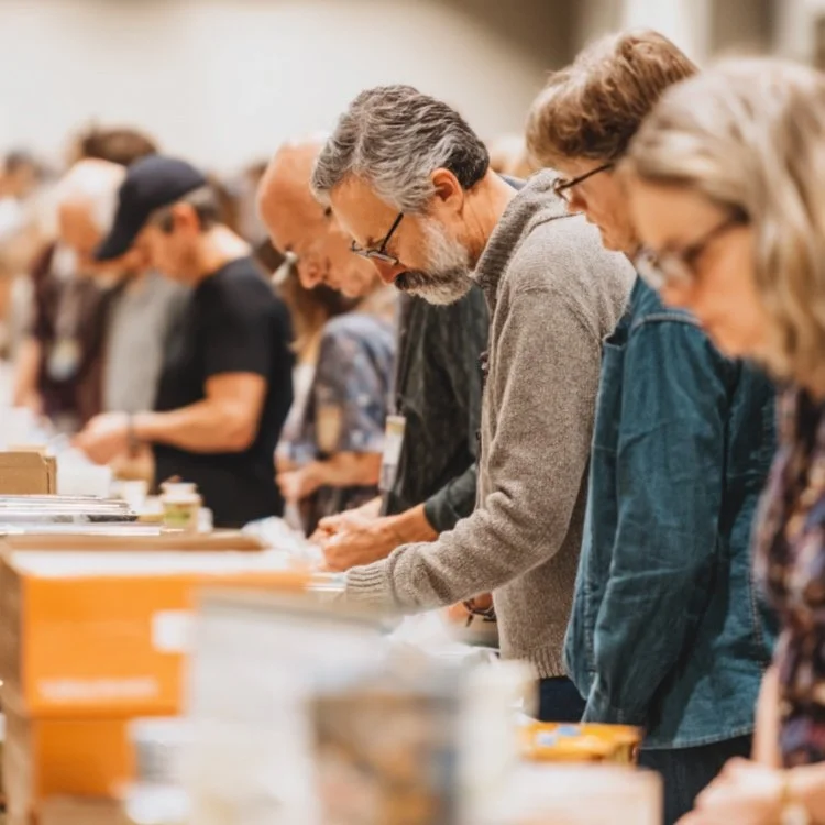 People standing in line at a book fair or event browsing through books.