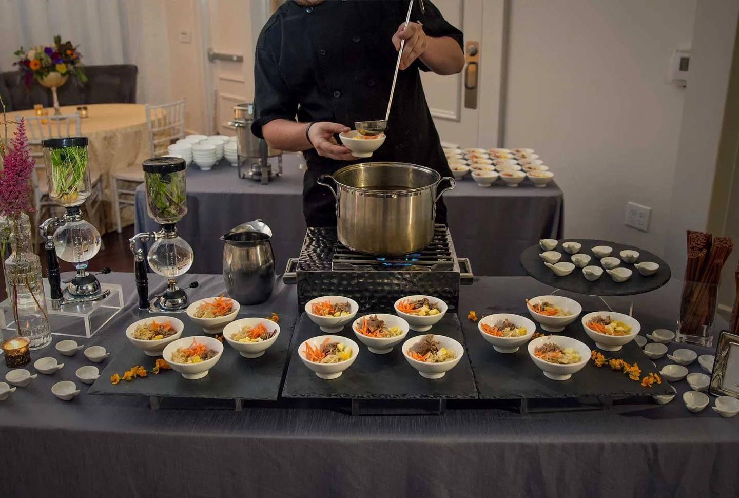 A chef preparing bowls of food at a buffet table, with bowls of ingredients and garnishes on display.